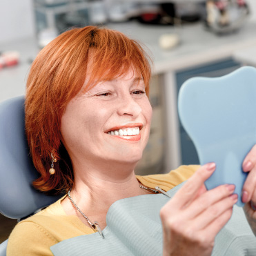 Mulher se olha no espelho, sorrindo, com dentes perfeitos.