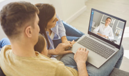 Família Pai, Mãe e Criança em frente a uma tela de notebook onde se vê médico da Telemedicina GNDI em atendimento.