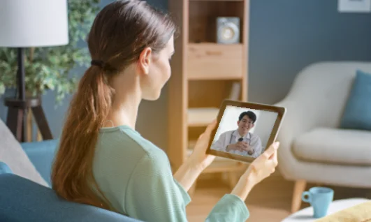 Mulher olhando a tela de seu tablet e participando de consulta via telemedicina