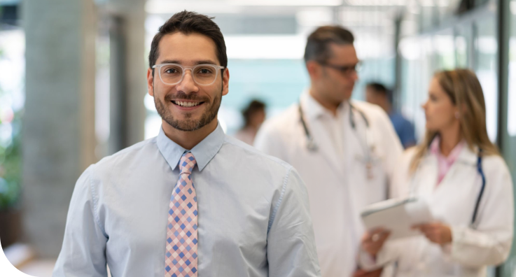 Homem de camisa social azul e gravata rosa com azul sorrindo.