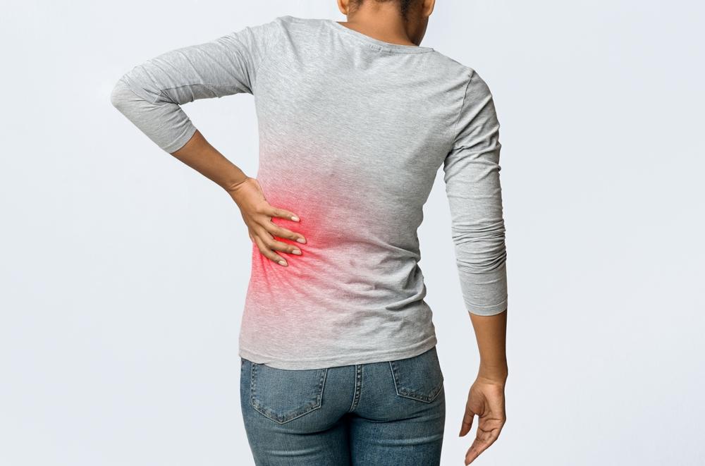 Mulher com a mão na região lombar destacada em vermelho, indicando dor típica de cálculos renais e a necessidade de avaliação para tratamento. Remoção de cálculo renal.